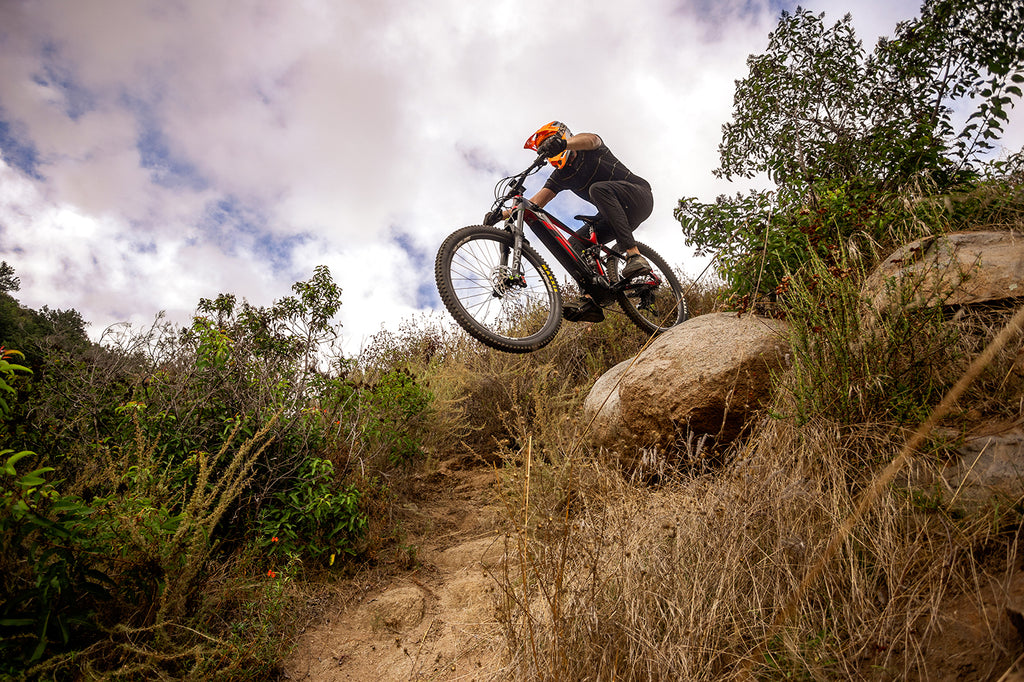 a Mountain biker riding a Superhuman Weapon X electric mountain bike off a large rock drop at a southern California Trail system