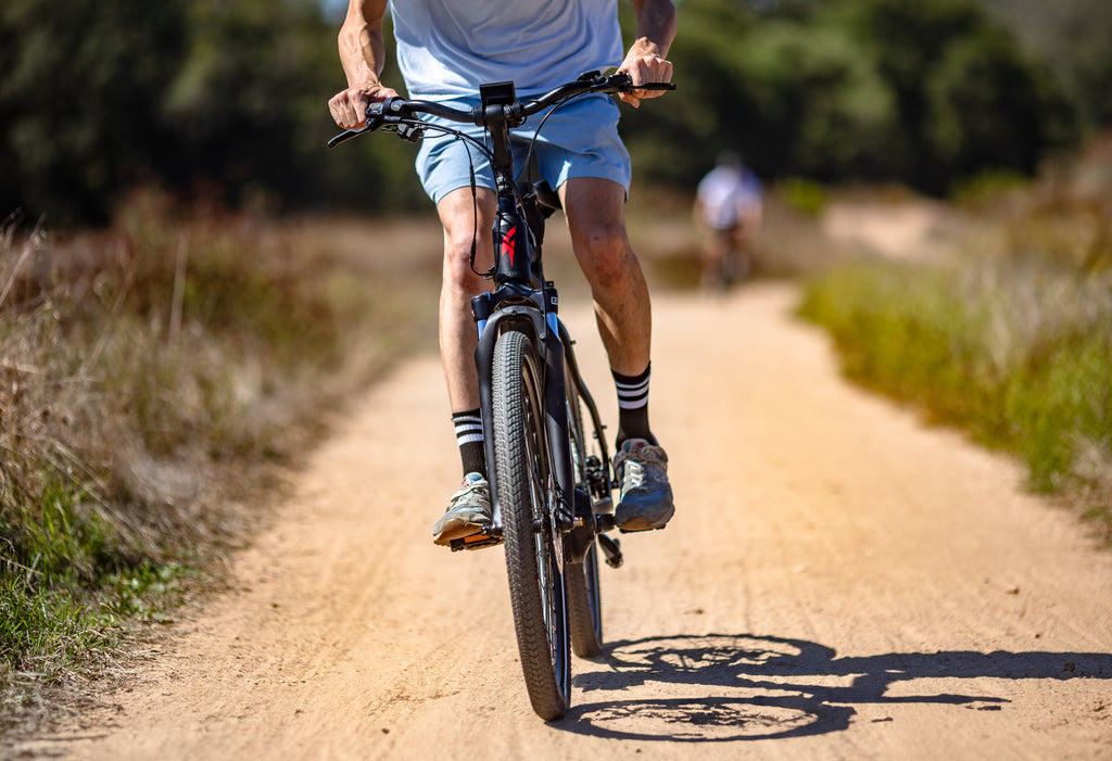 tight photo of a young man riding an FLX Step Through Electric comfort bike on an off road trail