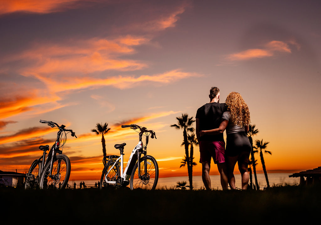 a man and woman watching the sun set over the Pacific ocean with two Superhuman electric bikes in the foreground