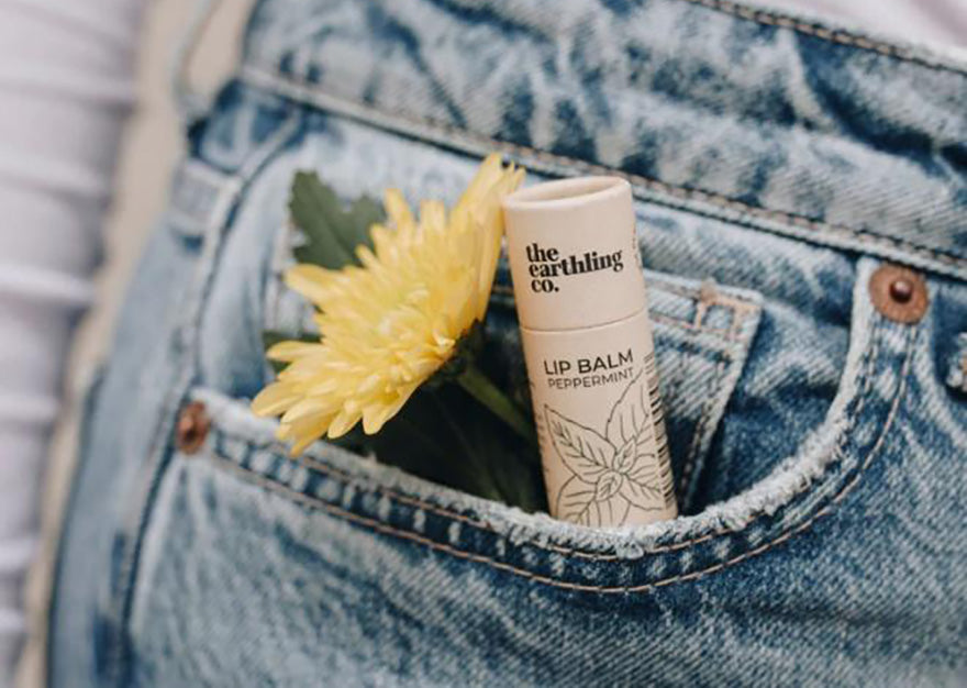 a tube of earthling co peppermint lip balm in a persons pocket with a flower