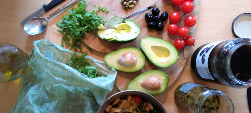 Avocado Tomatoes Capers Olives and rocket from a BeeBee Wrap on the chopping board ready for a salad