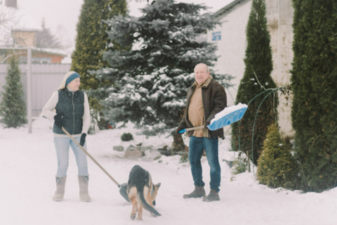 an older couple shoveling snow with their dog
