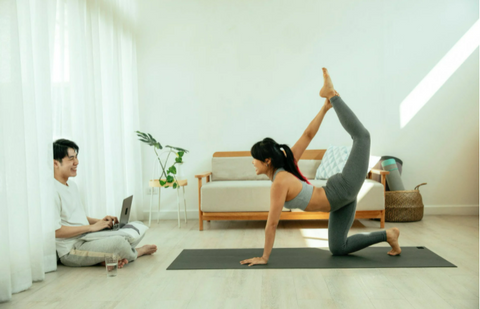 a couple doing hobbies together, one on a computer one doing yoga
