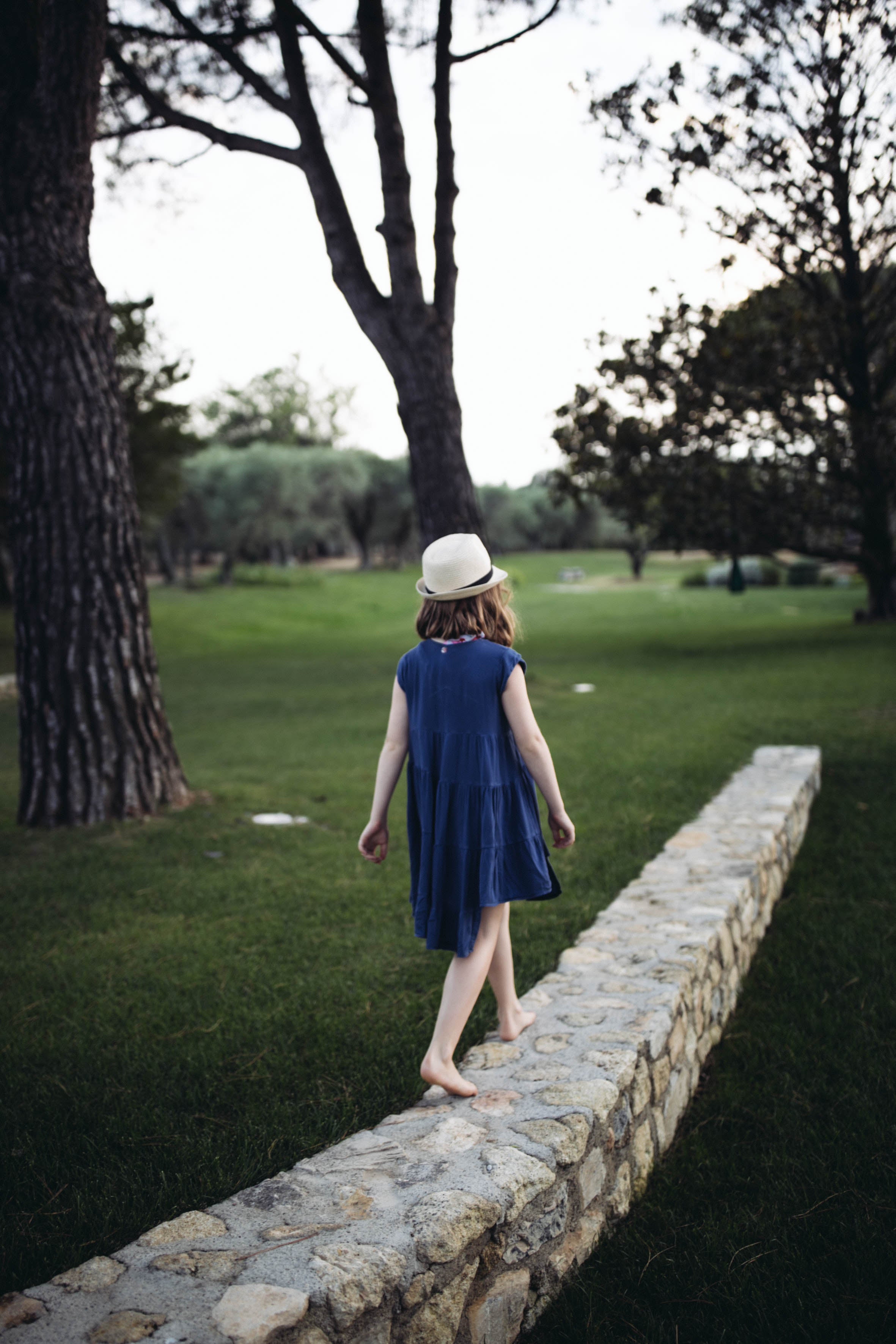 Girl walking barefoot along a stone wall wearing a hat