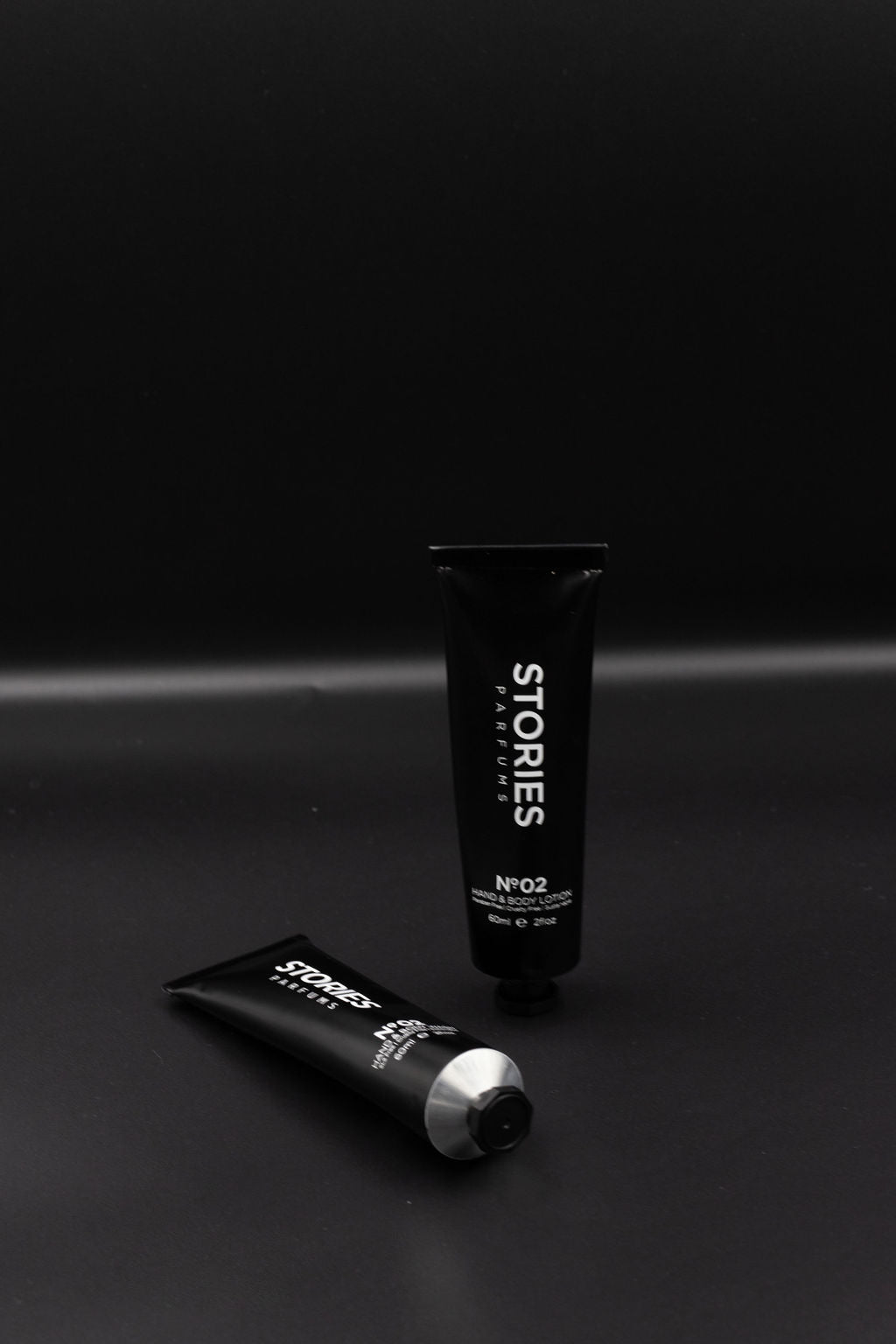 Black tubes of STORIES Hand and body lotion resting against a black background