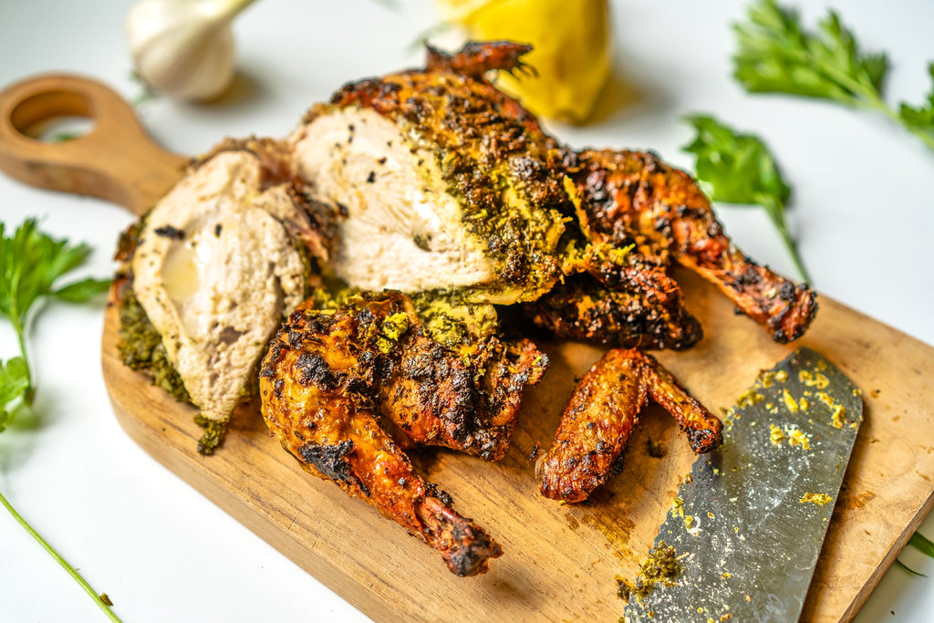 Roasted whole chicken with spices on a wooden cutting board. 