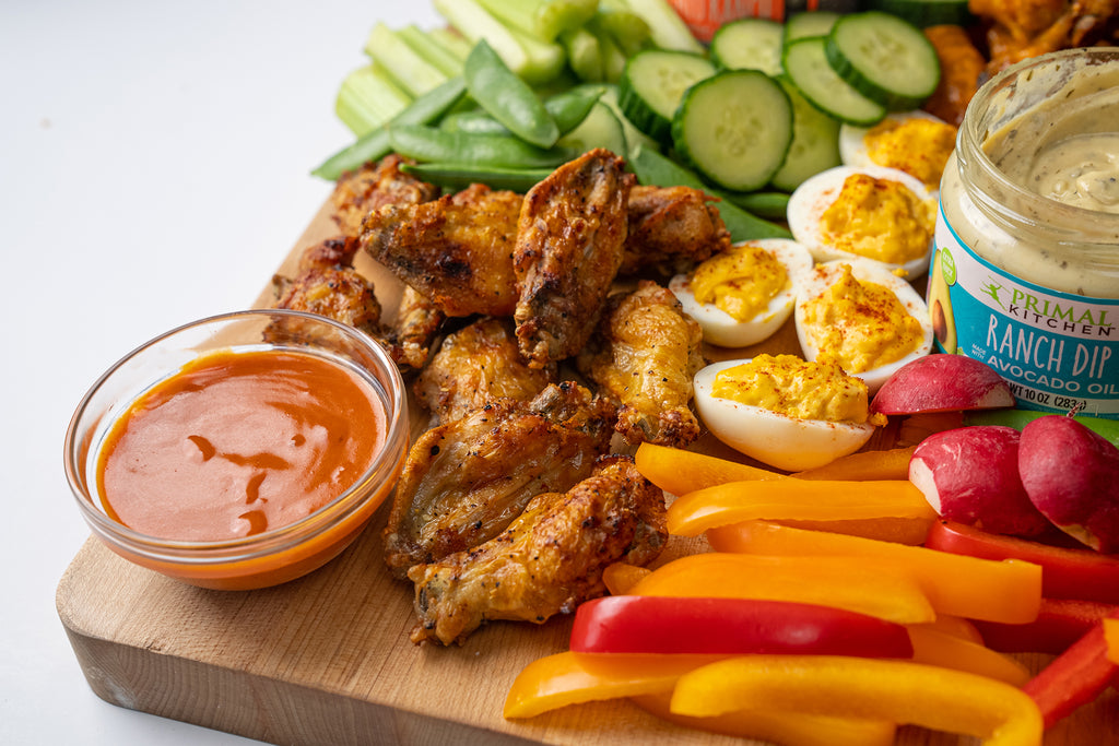 Veggies, wings, deviled eggs, and Primal Kitchen sauces and dips on a wooden charcuterie board.