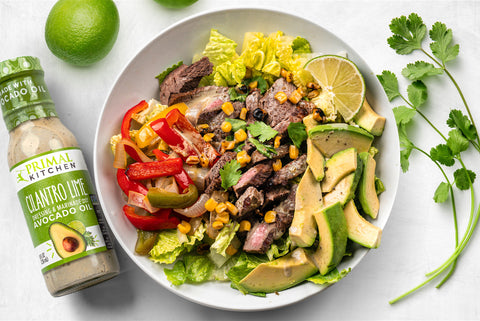 A bowl of salad topped with steak, fajita vegetables, and Primal Kitchen Cilantro Lime Dressing.