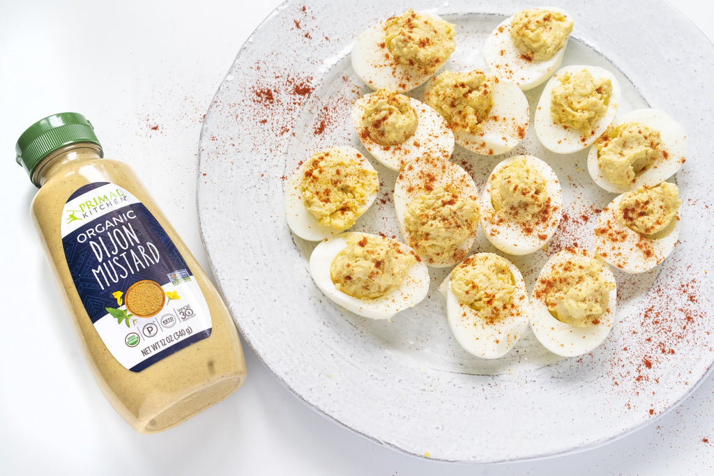 Deviled eggs on a white plate next to a bottle of Primal Kitchen Dijon Mustard