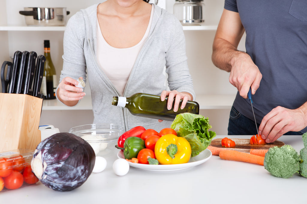 A couple cooking, with the woman adding oil to the food.