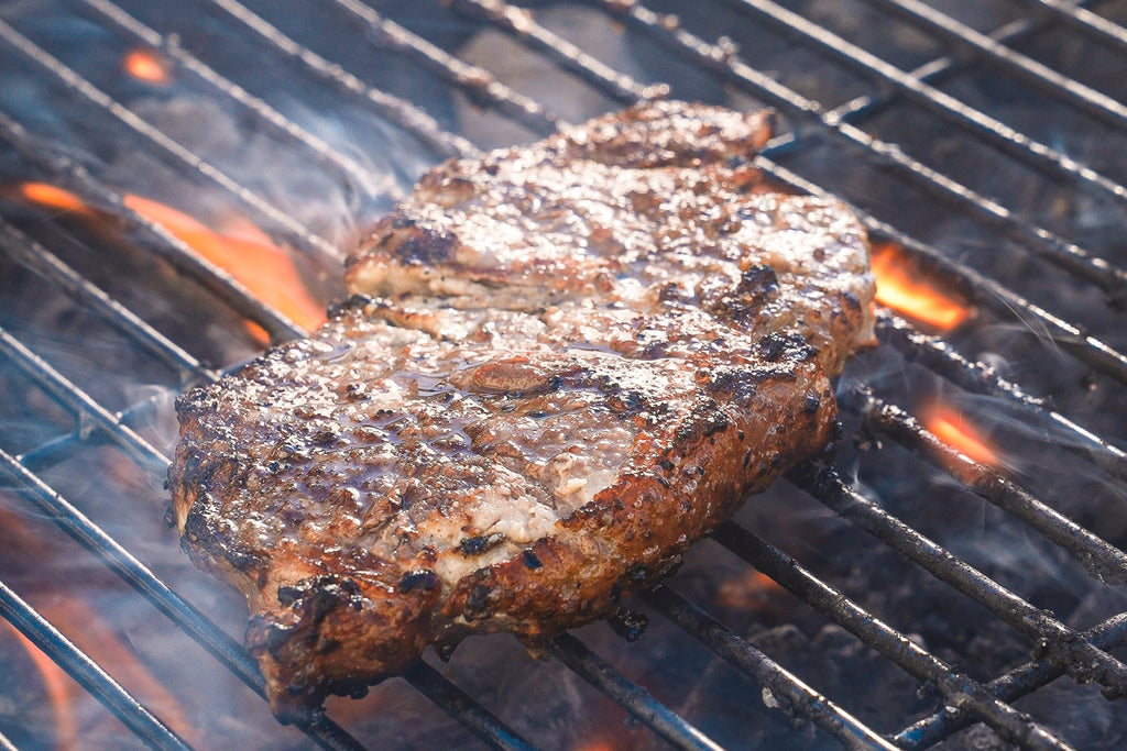 A juicy steak slathered in Primal Kitchen mayo on a BBQ grill.