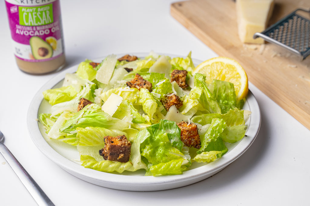 A plate of plant based caesar salad in front of a bottle of Primal Kitchen Plant Based Caesar Dressing