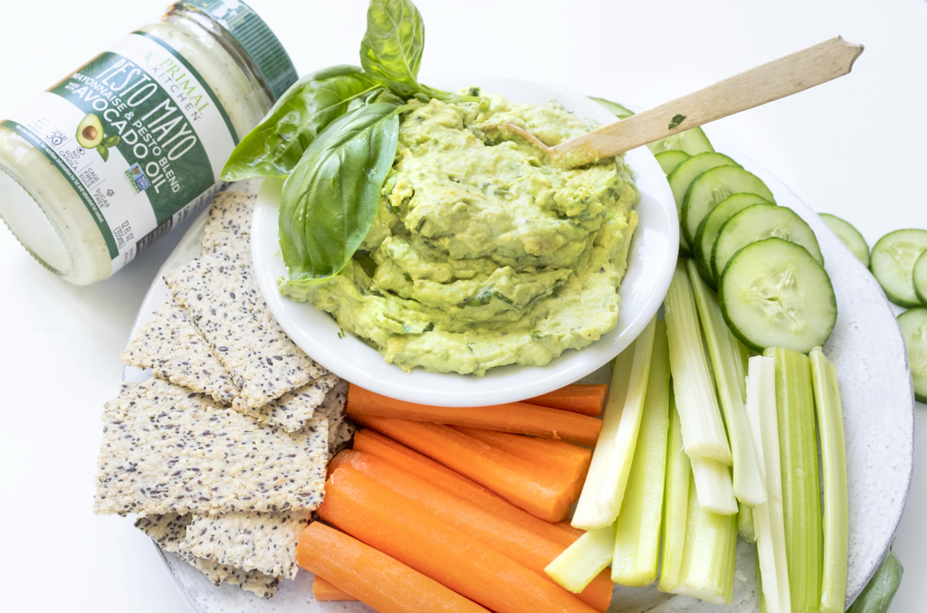 Creamy guacamole is surrounded by crudité and pesto mayo in the background.