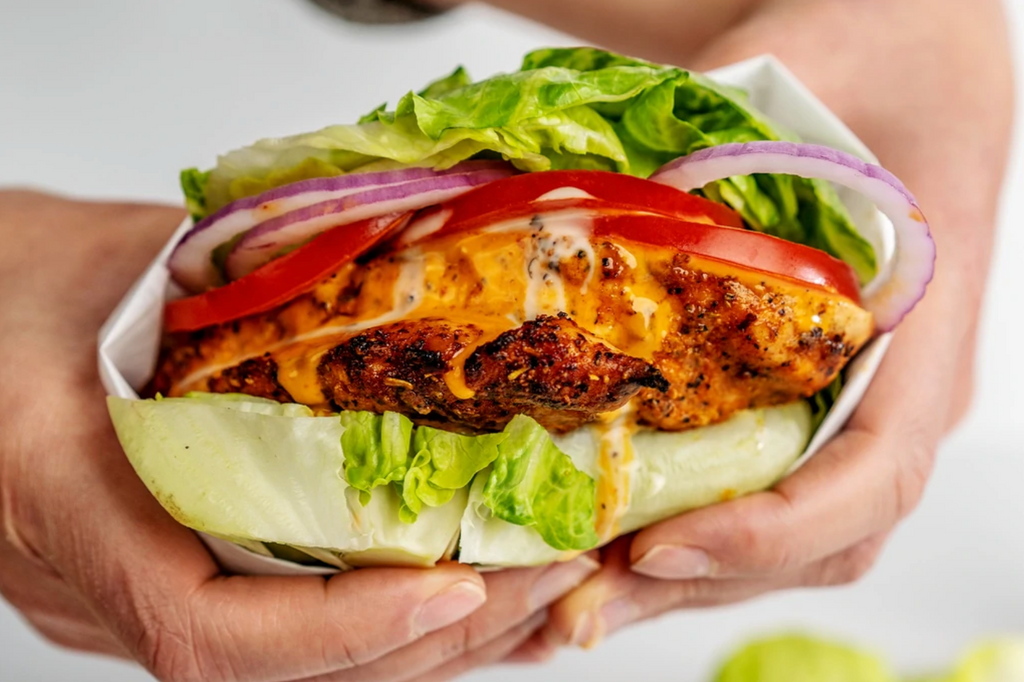 Two hands grasp a buffalo chicken sandwich wrapped in lettuce. 