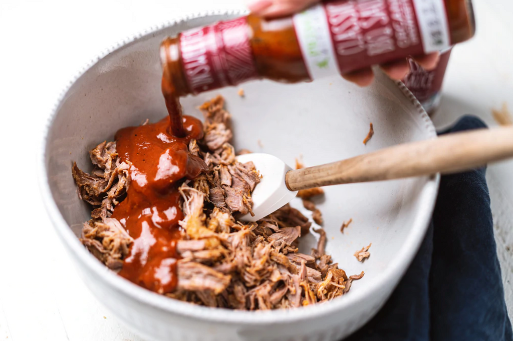 classic bbq sauce is being poured onto pulled pork.