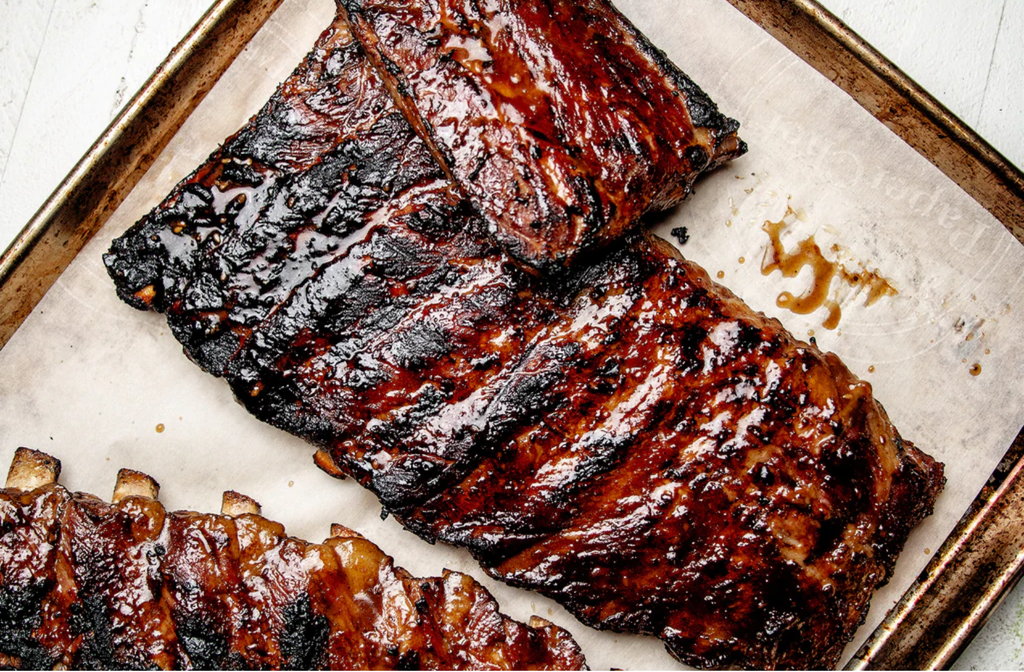 Sticky ribs are laid out on a pan with parchment paper.