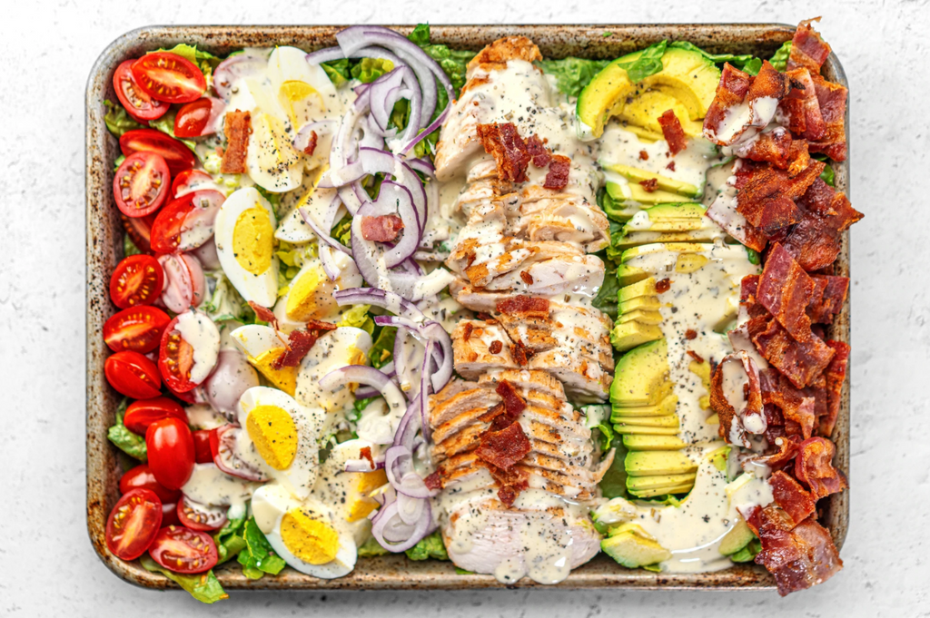 A sheet pan is filled with all the ingredients for keto cobb salad and is drizzled in ranch dressing.