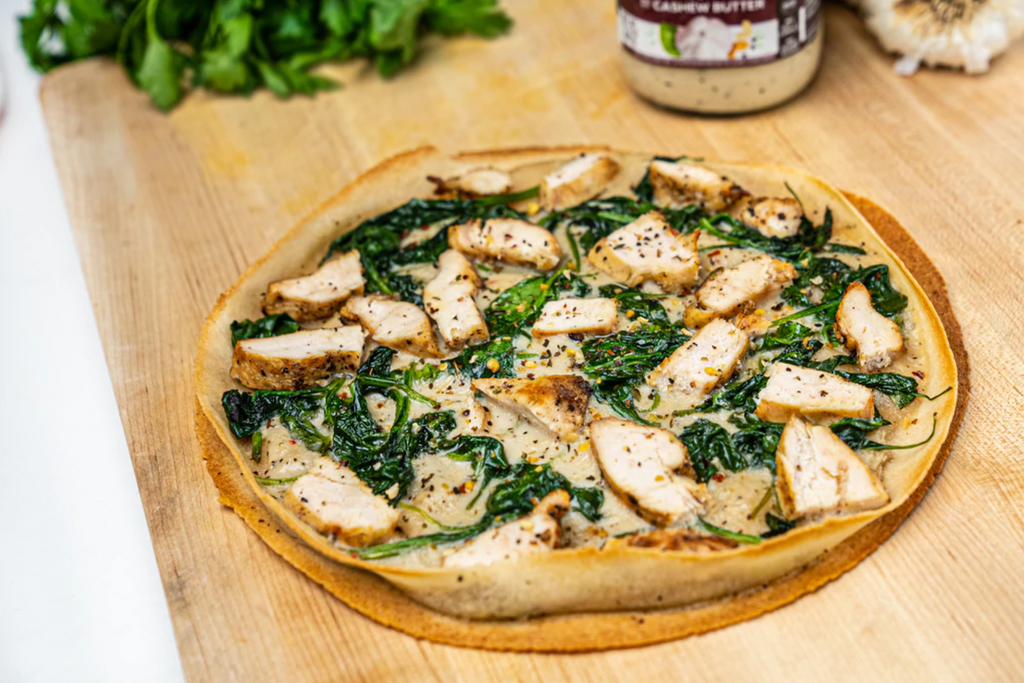 Chicken florentine pizza is on a cutting board with ingredients behind it and nearby.