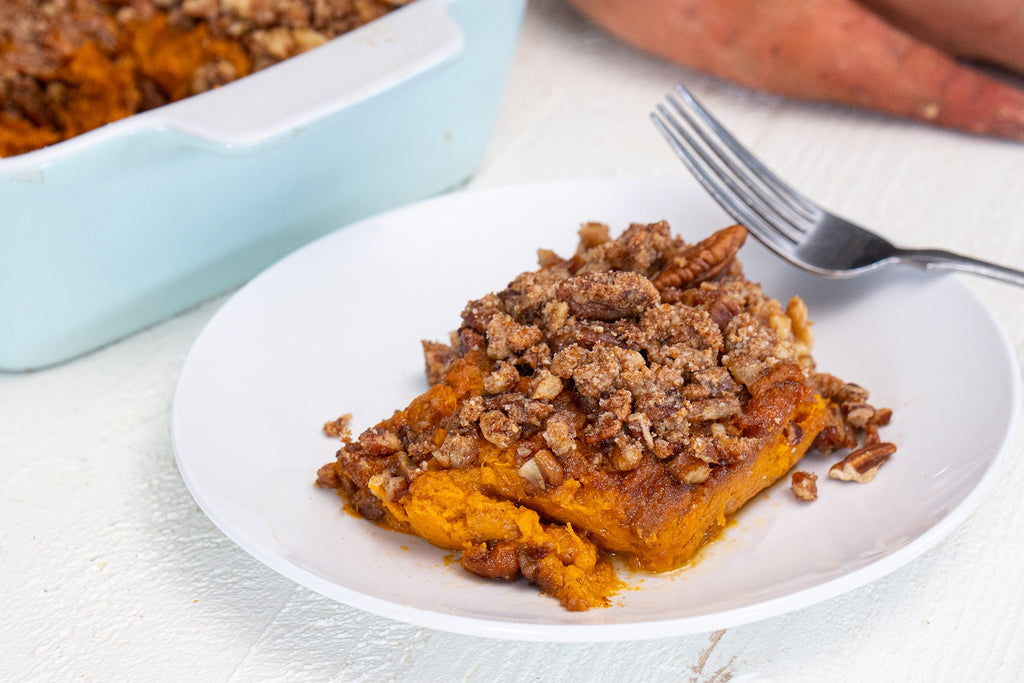 A serving of sweet potato casserole on a white plate, with a baking dish in the background. 
