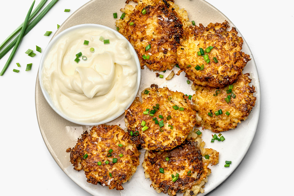 A white plate has cauliflower fritters arranged around a ramican of vegan mayo.