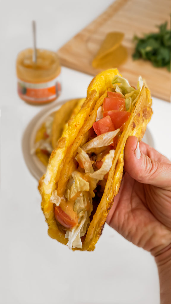 A cheesy Gordita Crunch wrap being held with queso dip in the background.