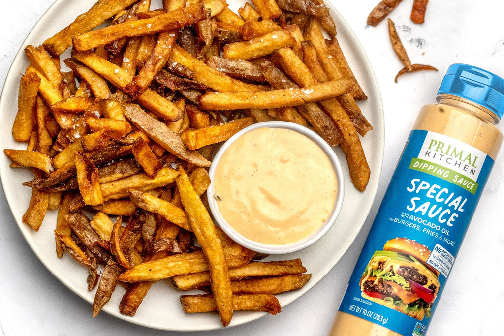 A plate of fries next to a bottle of Primal Kitchen Special Sauce.