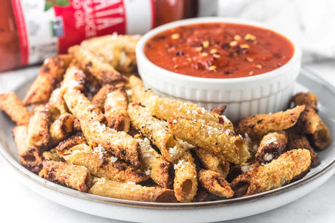 A plate of air-fried gluten-free penne pasta "chips" with a ramekin of Primal Kitchen Arrabbiata Sauce for dipping. 