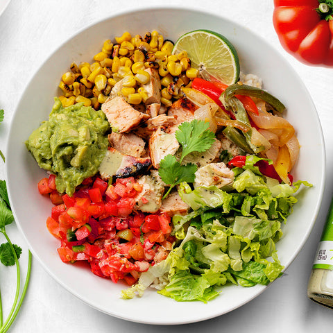 A burrito bowl with grilled chicken, fajita vegetables, roasted corn, guacamole, and Primal Kitchen Cilantro Lime Dressing. 