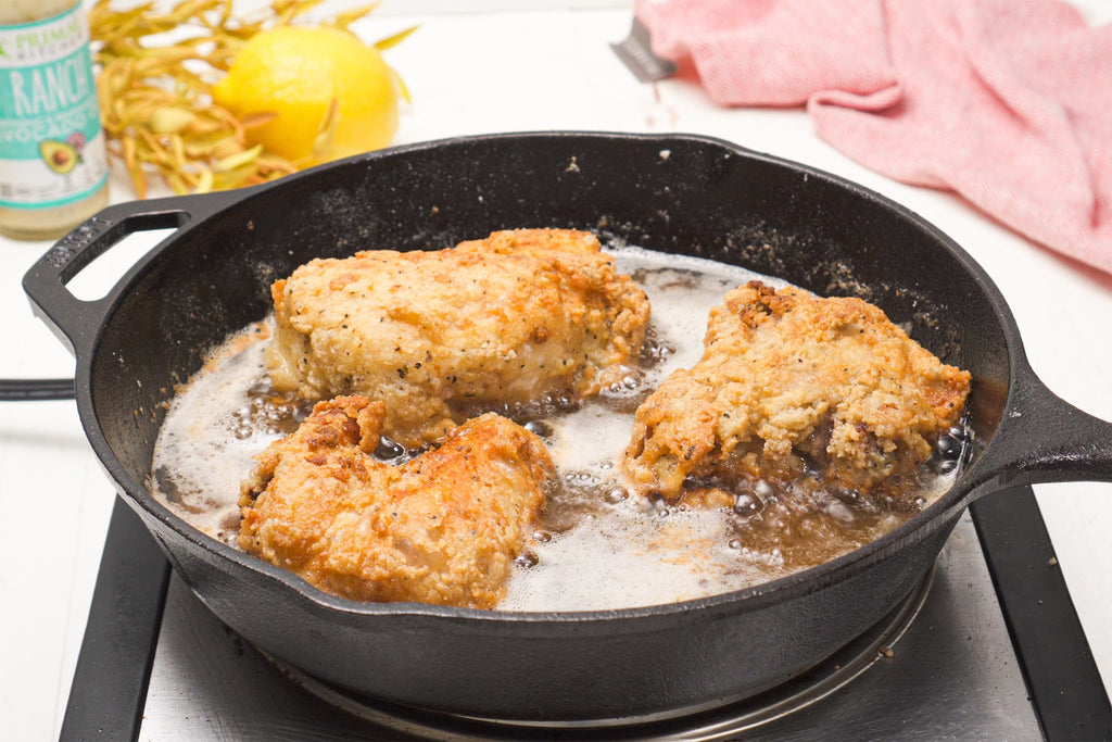 A skillet of bubbling fried chicken cooking in Primal Kitchen oil.