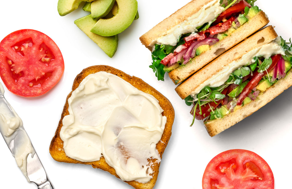 Slice of toasted bread slathered with Primal Kitchen Mayo next to a Vegan Mayo Veggie Sandwich