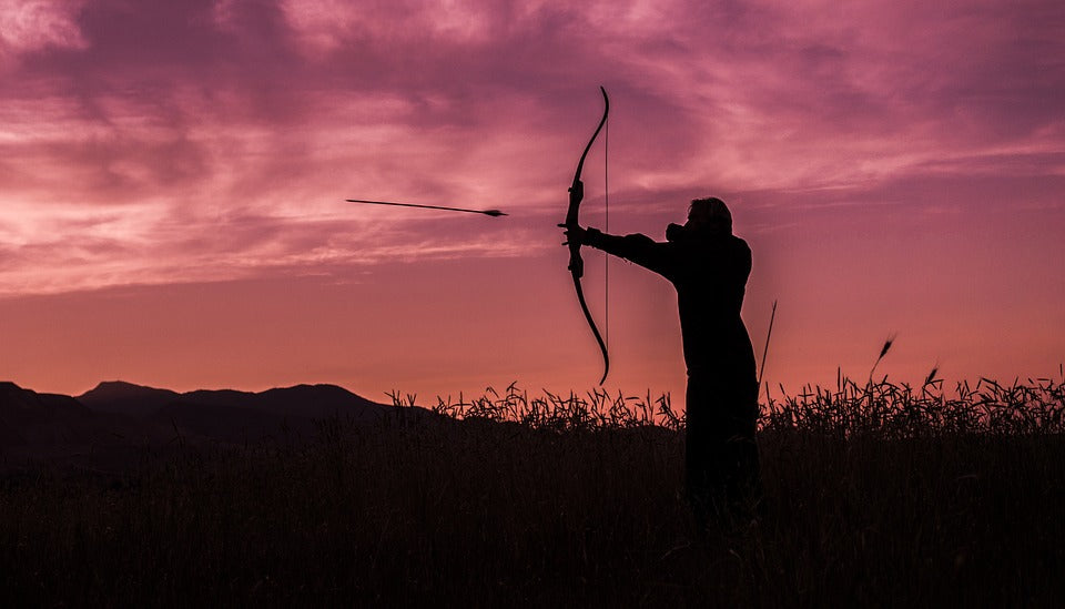 An archer firing an arrow at sunset