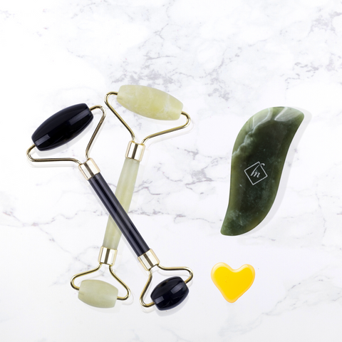 Image of two stone facial rollers (in green and black)and a jade gua sha with a heart-shaped drop of oilon well&belle