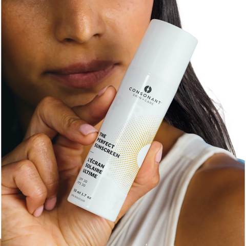 Image of woman with dark skin and long dark hair holding bottle of The Perfect Sunscreen by Consonant on well&belle.