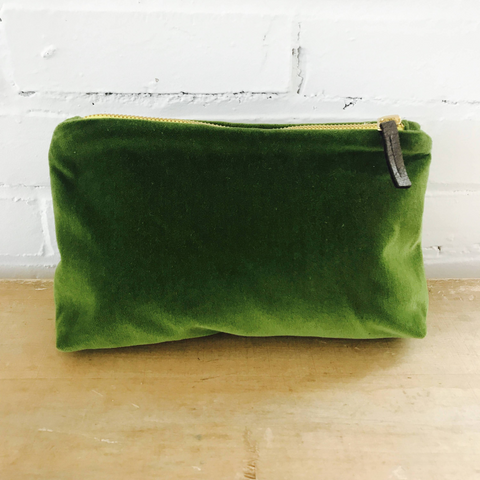 Image of large green velvet cosmetic bag on wood counter with white brick background. On well&belle