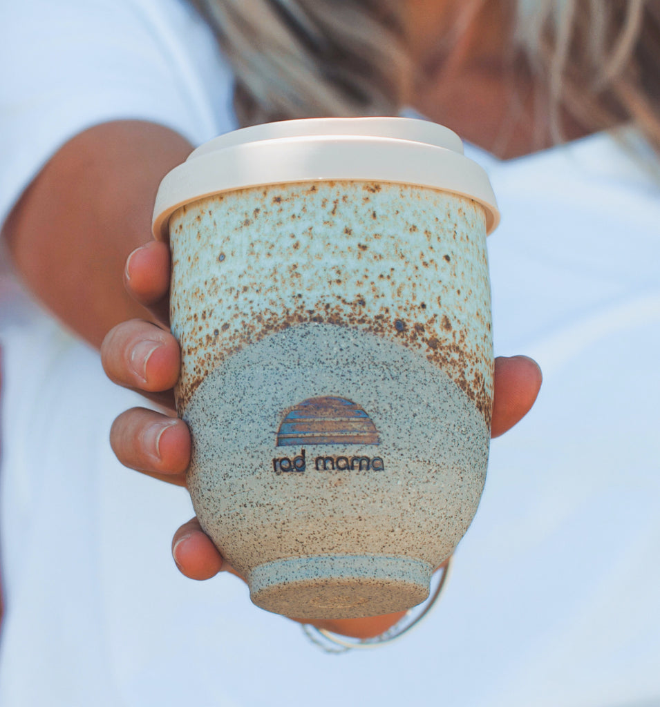 Woman holds out ceramic travel cup with rad mama logo