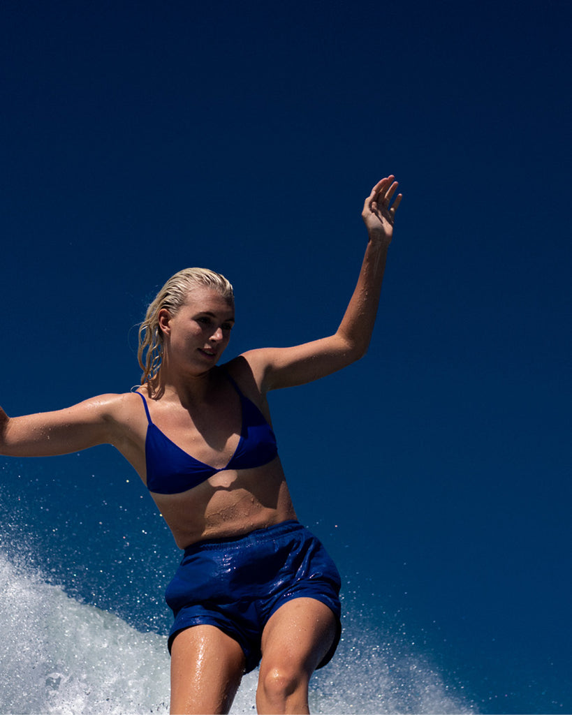 Mia surfing in a blue hakea bikini that matches the blue sky behind her