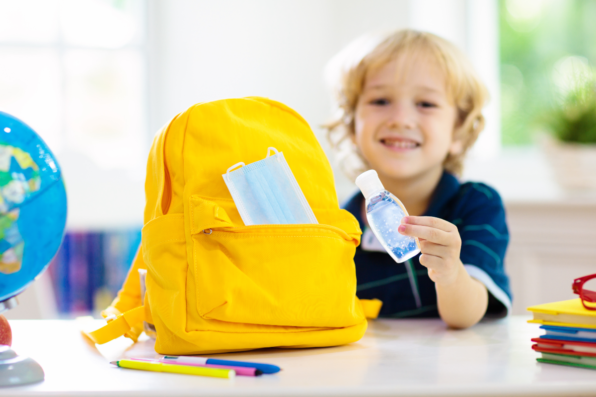  Smiling child prepares yellow backpack with back to school supplies. Keep back to school stress low with these tips.