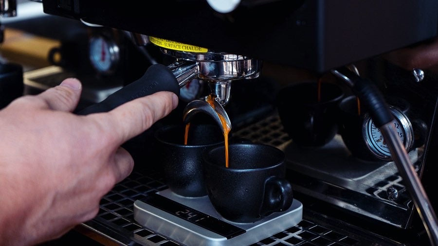 Double shot of espresso split is being split between two cups on a silver Lunar scale.