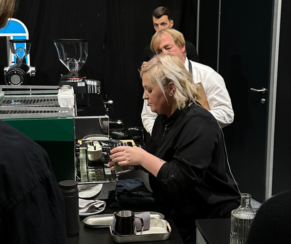 Barista Dominika Piotrowska steaming milk on an espresso machine surrounded by judges at the Austrian Barista Championships 2023