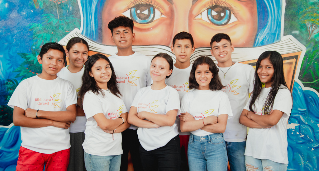 Children with "Biblioteca Girasol" t-shirts standing in front of a brightly colored mural. Photo by Esquil Rocha