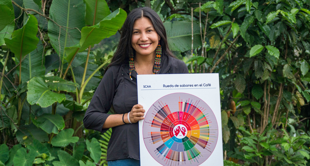 A Chain collaborative member standing with an SCA Flavor wheel in front of some foliage. Photo by Witoca Coffee