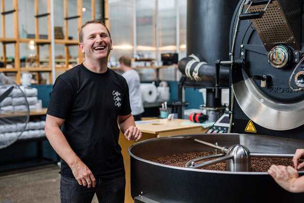 Espresso Workshop owner standing in front of a large coffee roasting machine