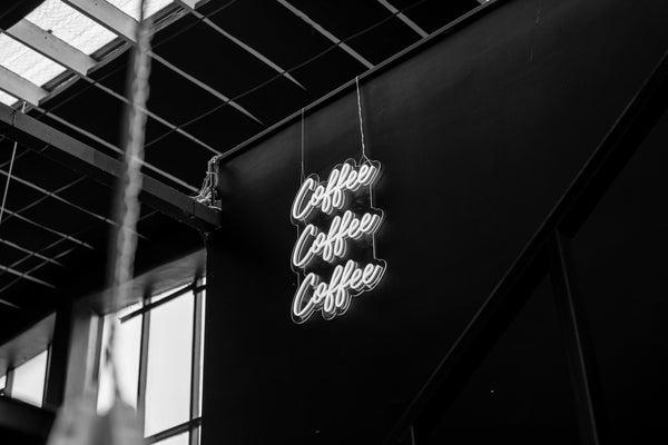 A black and white image of a neon lamp spelling "coffee coffee coffee" on a wall