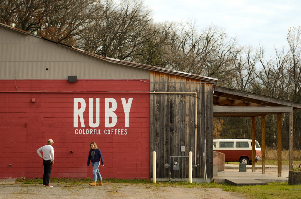 Two people infront of a red building with 'Ruby' written on the side 