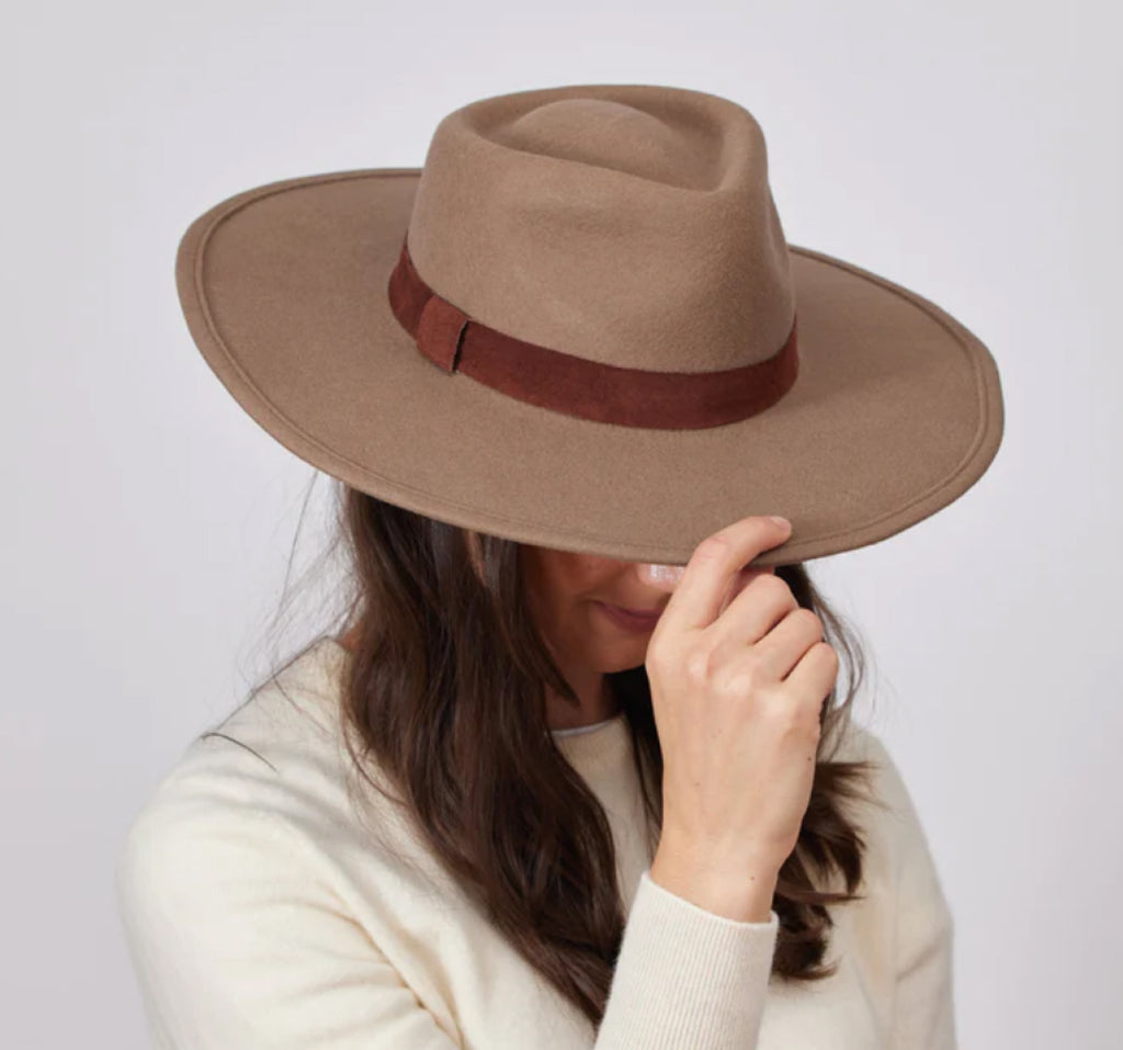 Woman wearing and holding brown felt hat with tim.