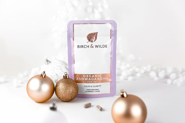 pack shot lifestyle image of a stand up refill pouch of Birch & Wilde Organic Ashwagandha KSM-66 capsules, with a white background and surround by gold and white Christmas baubles and decorations