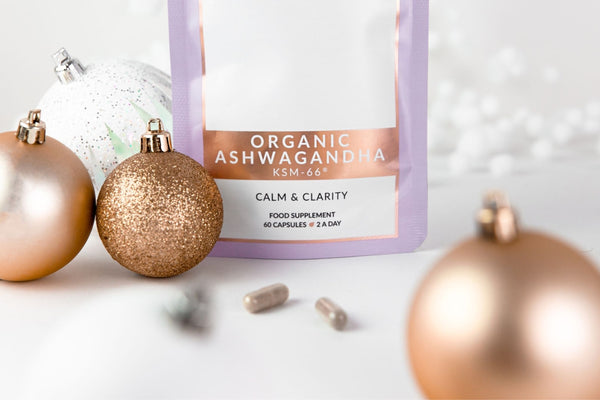 close up lifestyle image of a stand up refill pouch of Birch & Wilde Organic Ashwagandha KSM-66 capsules, with a white background and surround by gold and white Christmas baubles and decorations