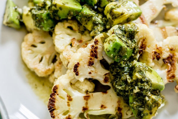 Chargrilled cauliflower steaks drizzled with homemade green avocado chimichurri dressing  on a white plate and viewed from above