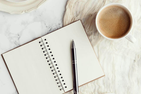 open mindfulness and wellbeing journal on a white marble table top with a cup of coffee and a gold pen