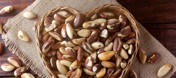 An image take from above of a brown heart shaped bowl filled with brazil nuts